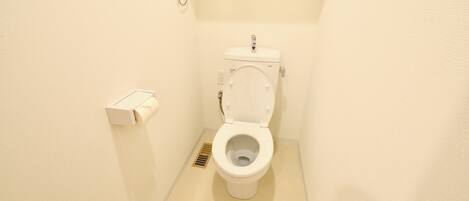 A small, clean bathroom with a toilet, a toilet paper holder, and a floor drain.