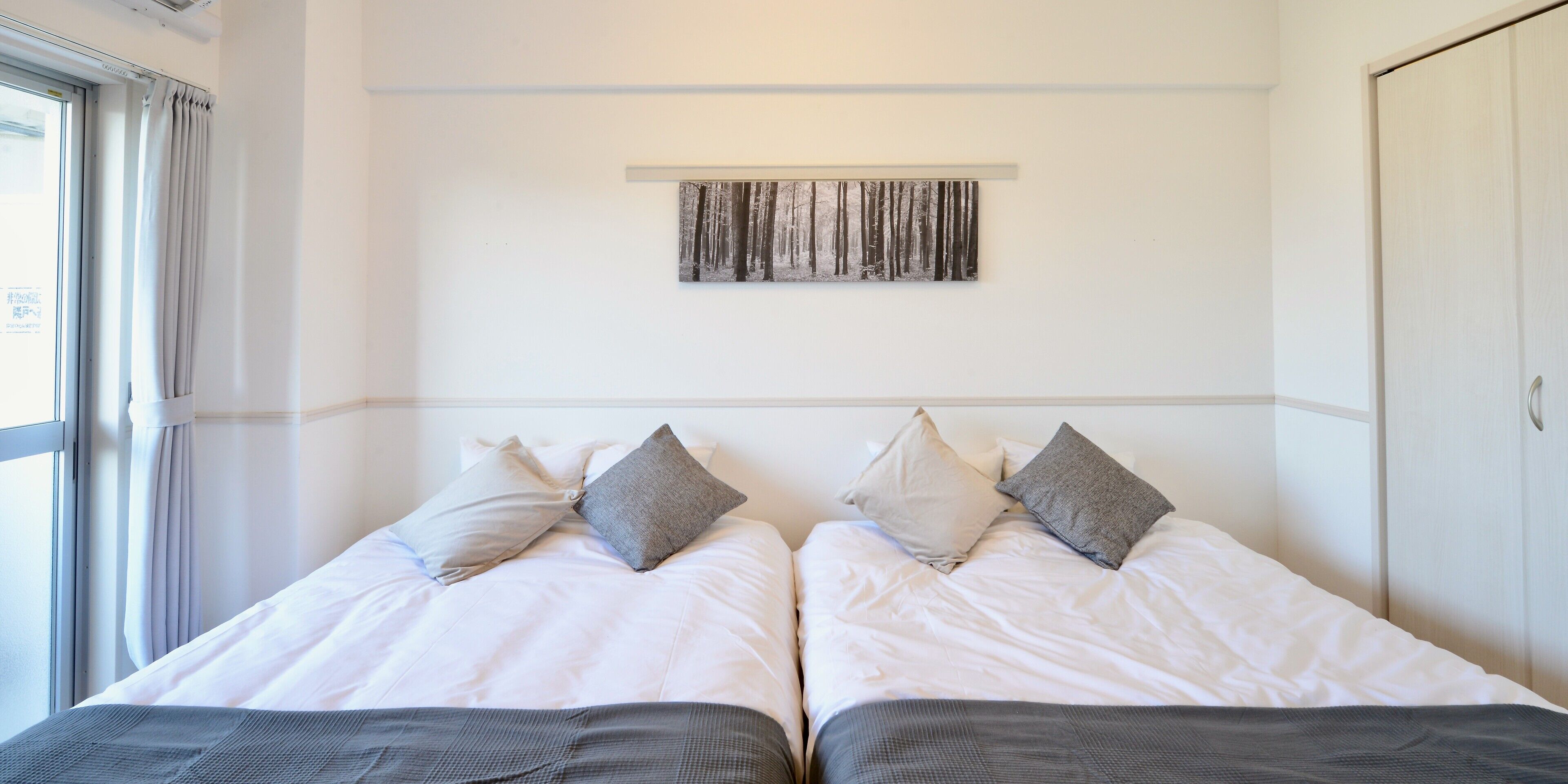 Una habitación de hotel con dos camas, una ventana, una obra de arte en la pared y un armario.