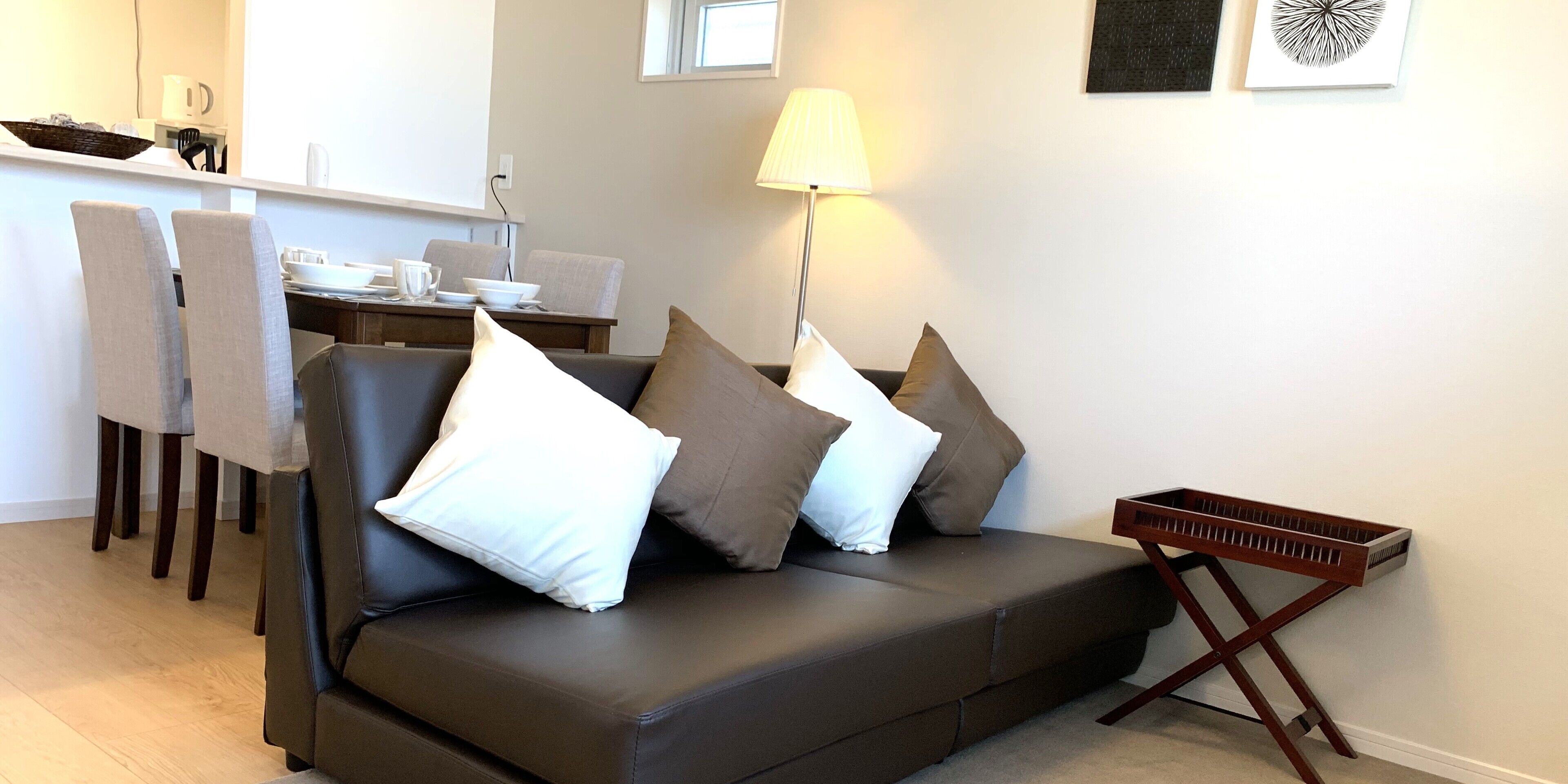 A modern living room with a brown leather sofa, a dining area with chairs, a lamp, and a keyboard on a stand.