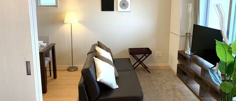 A living room with a sofa, a TV stand, a lamp, and artwork on the wall.