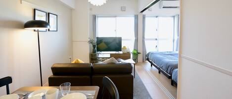 Una habitación de hotel compacta con zona de comedor, sofá, cama y televisor.