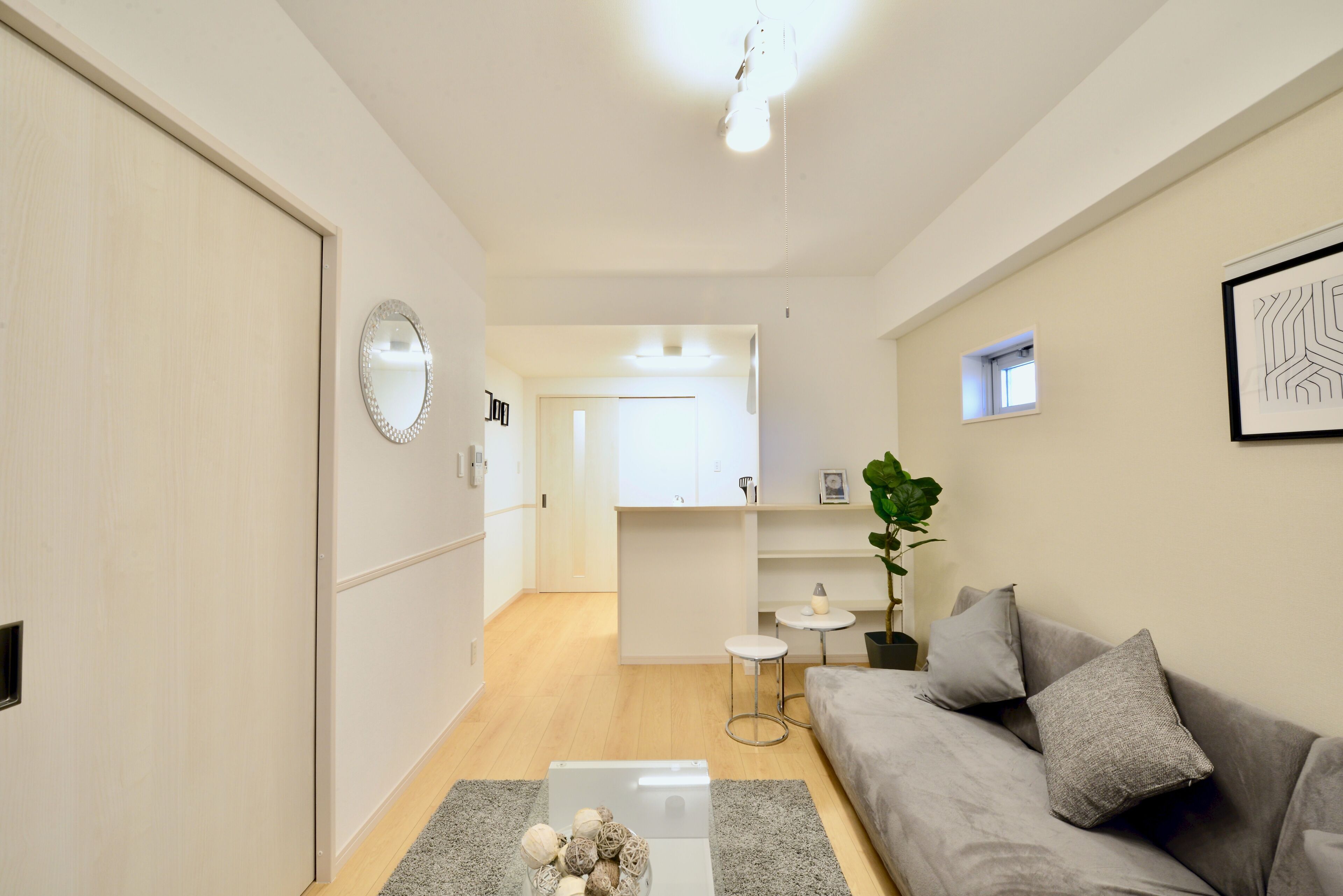 A modern living room with a grey sofa, a coffee table, and a small side table. There is a mirror on the wall and a plant on the side table.