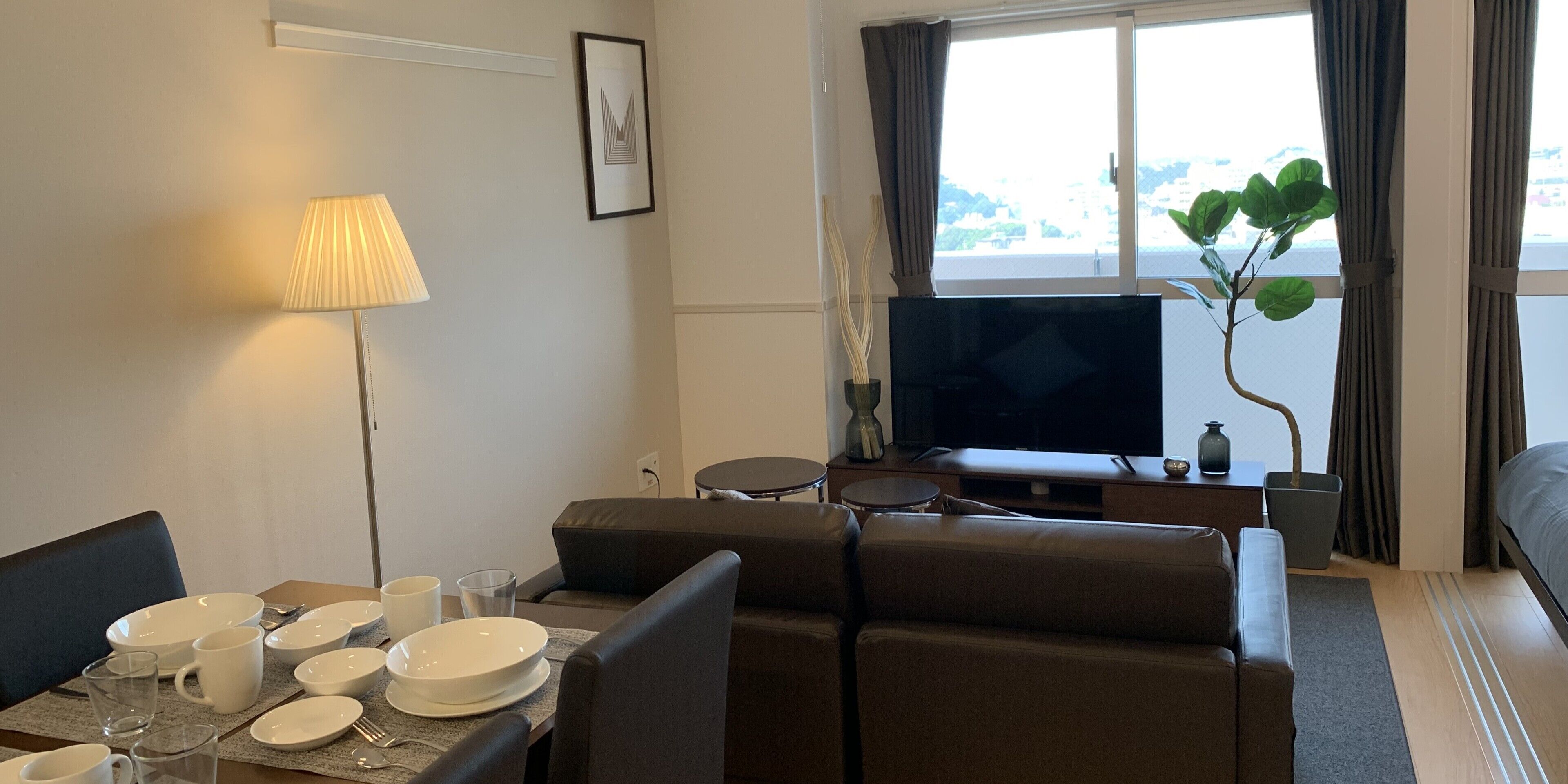 Une chambre d’hôtel moderne dotée d’un coin repas, d’un canapé, d’une télévision et d’une grande fenêtre avec des rideaux.