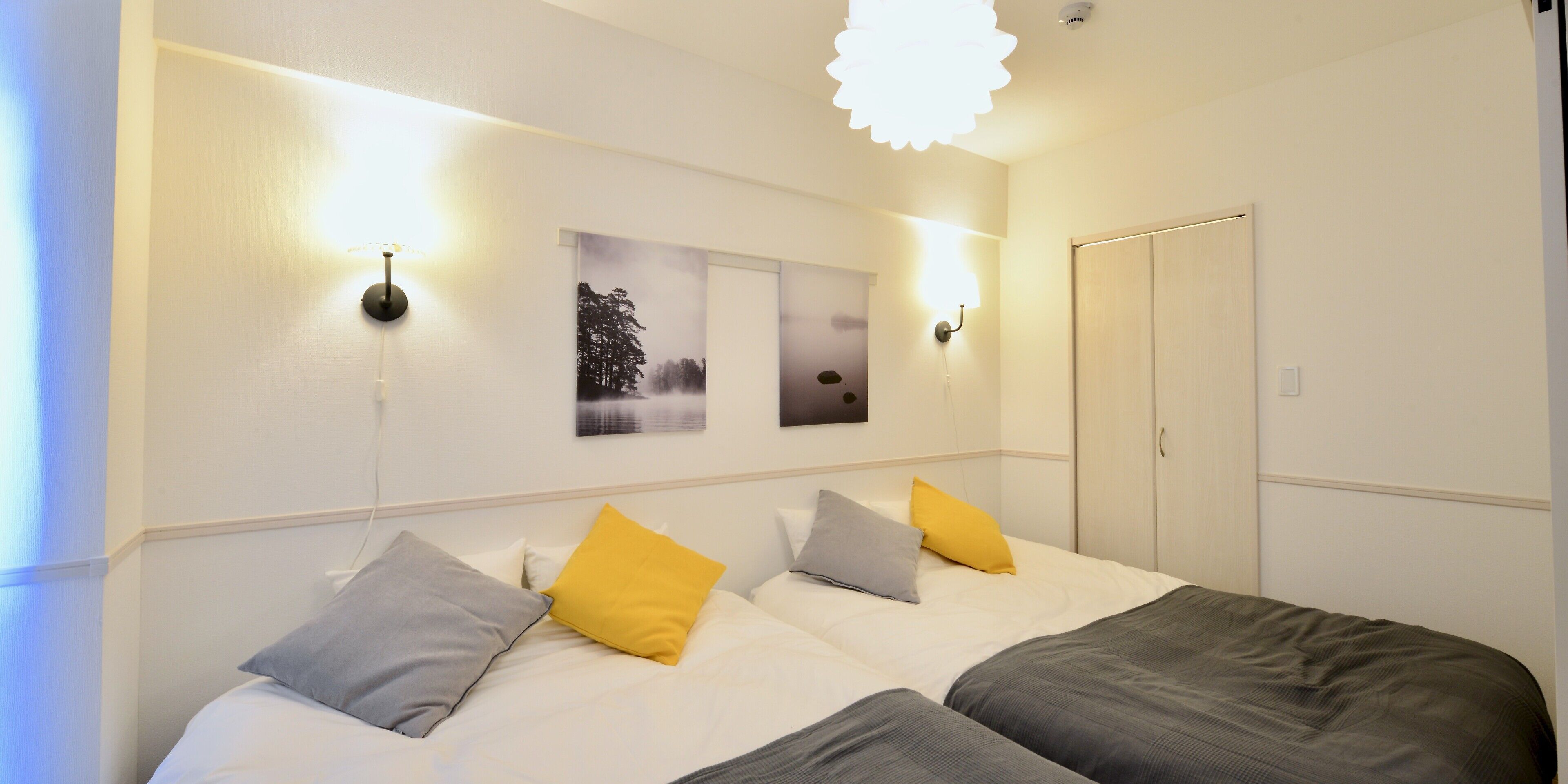 A hotel room with two beds, each with a pillow, a nightstand, a wall-mounted lamp, and a door.