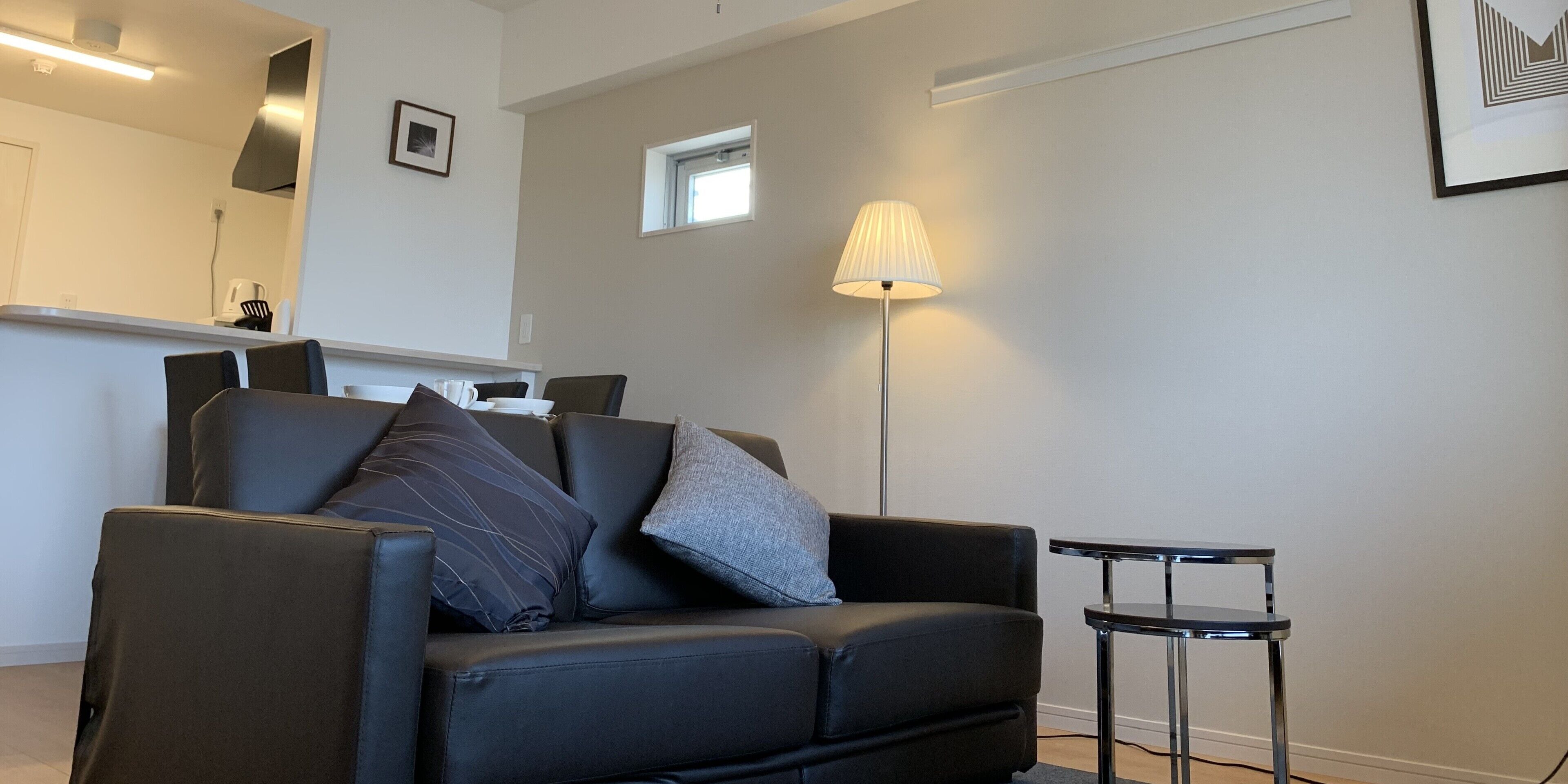 A modern living room with a black leather sofa, a small side table, and a floor lamp.