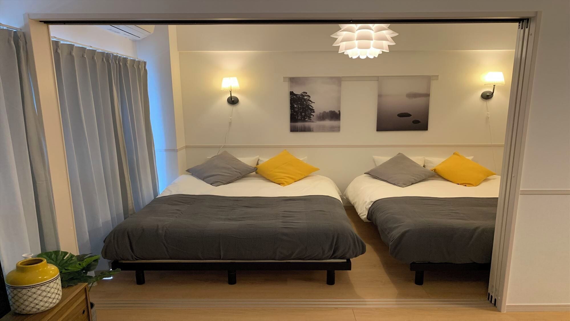 Ein Hotelzimmer mit zwei Betten, einem Nachttisch, einer Topfpflanze und Wandlampen.