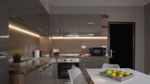 Una cocina moderna con horno empotrado, microondas y cafetera. Hay una mesa de comedor con una bandeja de frutas.