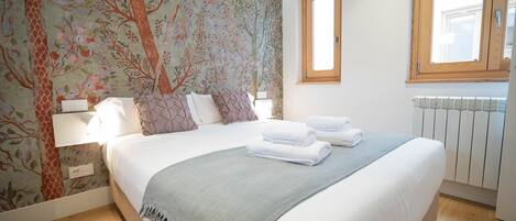 Una cama bien hecha con sábanas blancas y un plaid gris, cabecera de madera y diseño de papel tapiz floral.
