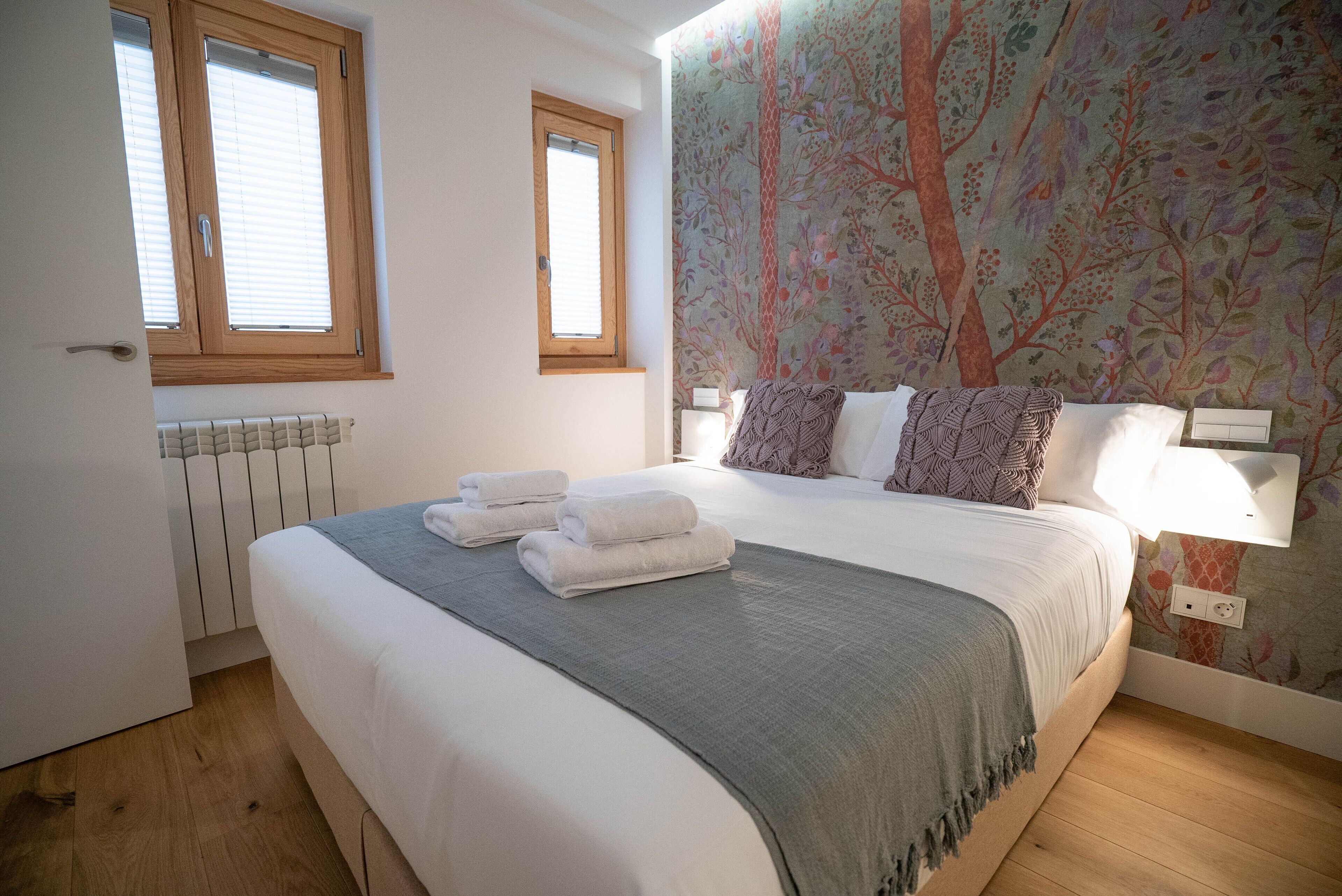 Quarto com cama, duas janelas, radiador e papel de parede floral.