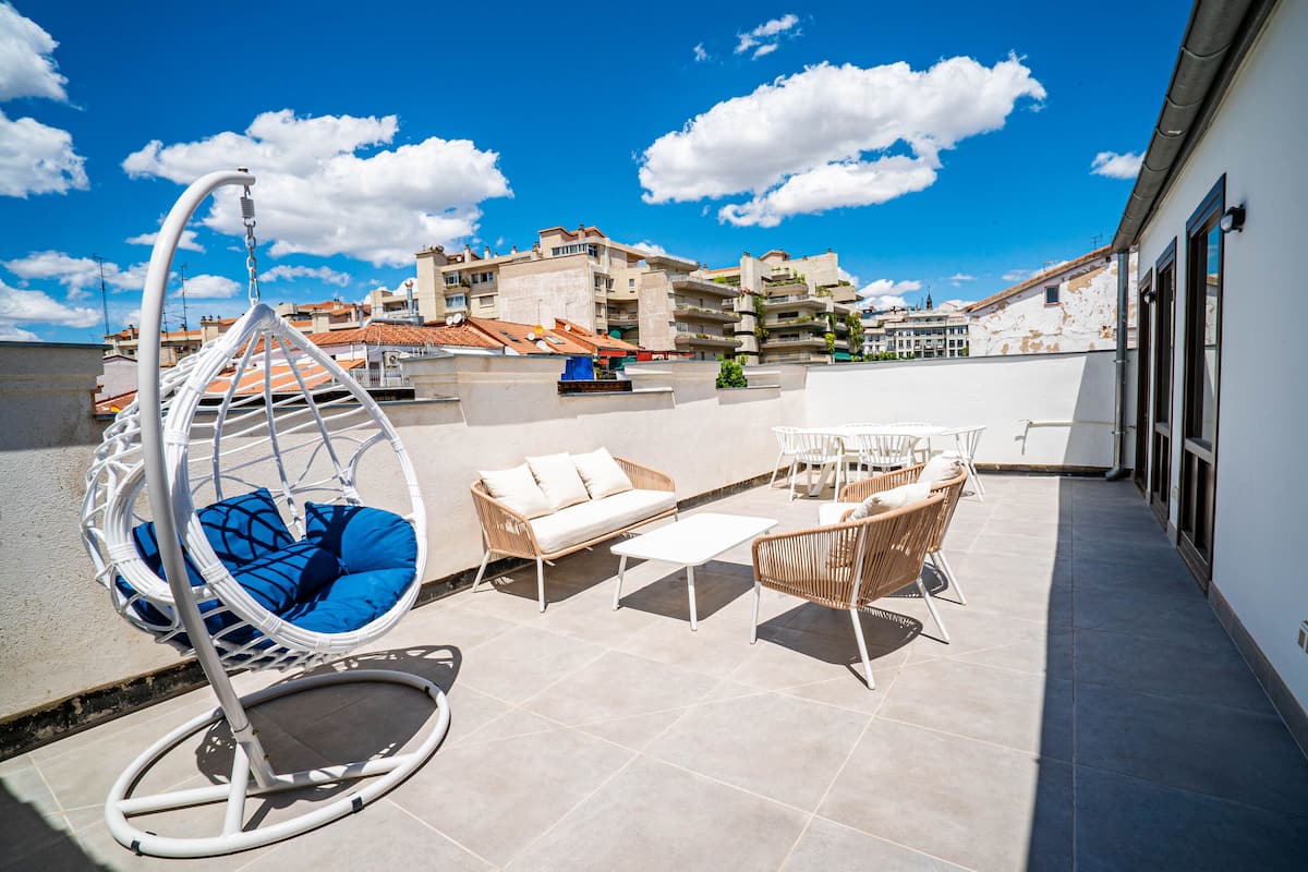 A rooftop patio with a hanging chair, sofa, and dining set.