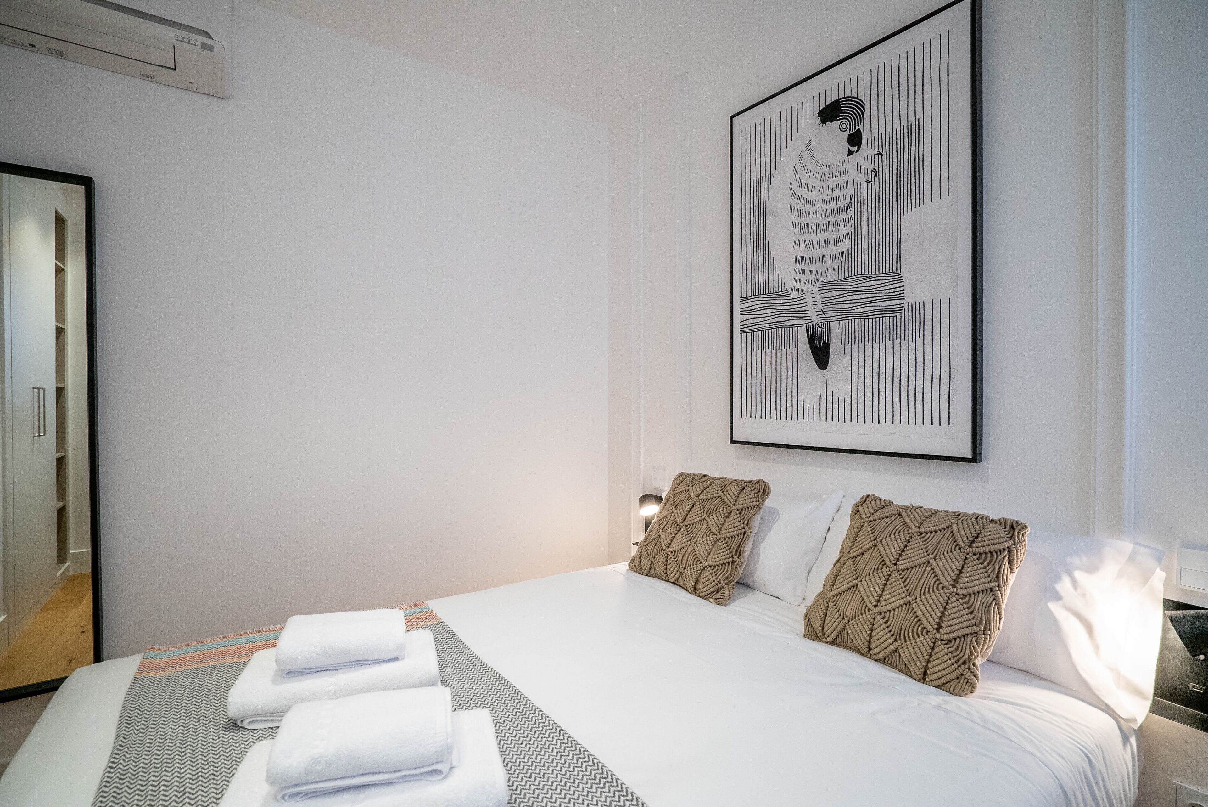 Ein Hotelzimmer mit einem großen Bett, weißer Bettwäsche, einem gerahmten abstrakten Kunstwerk und einer gemusterten Tagesdecke.