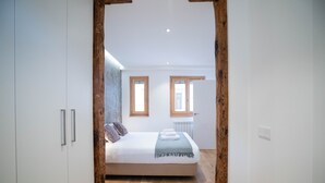 Une chambre à coucher avec un lit, un plancher en bois, des murs blancs et deux fenêtres.