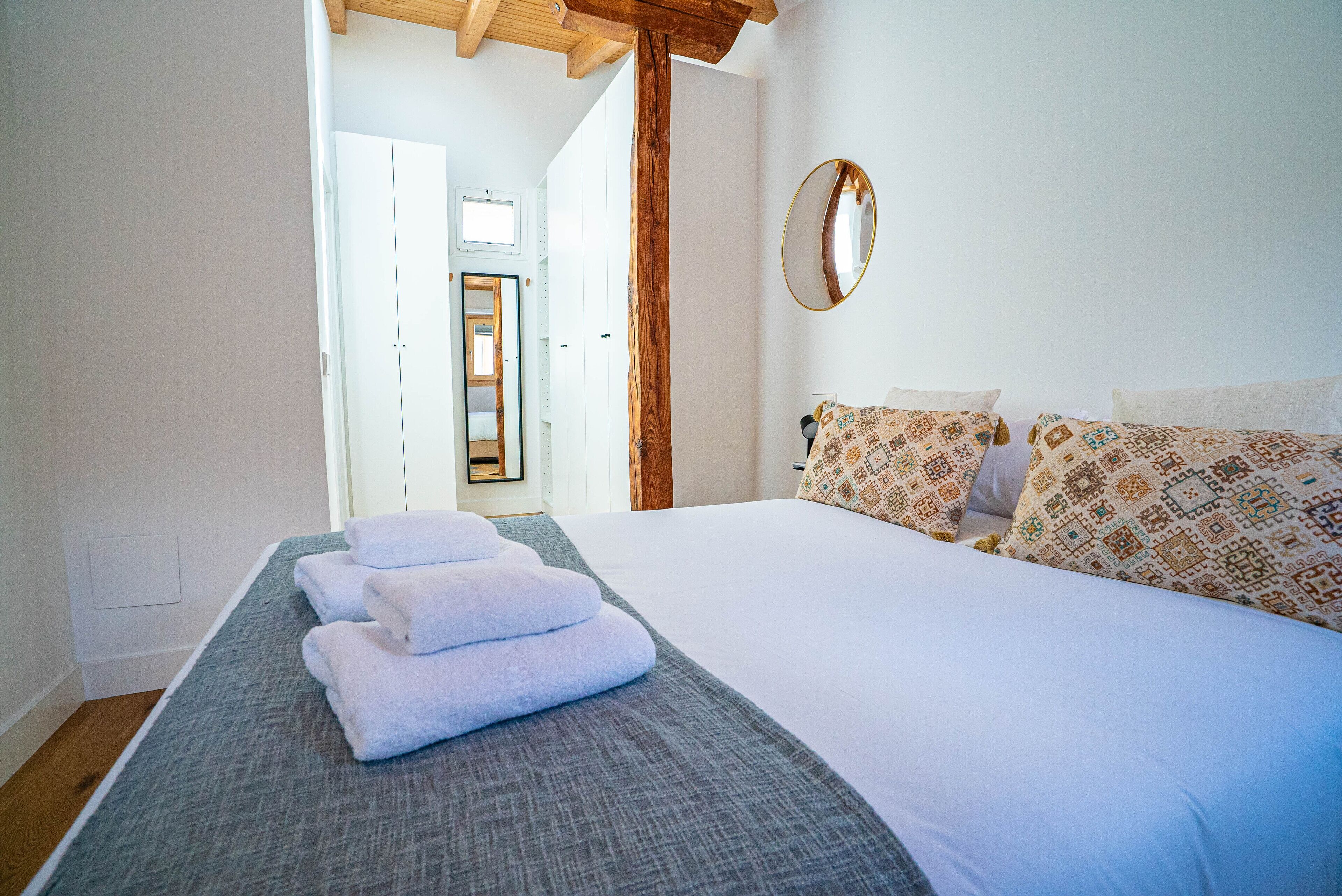 A hotel room with a bed, a mirror, and a view of a hallway.