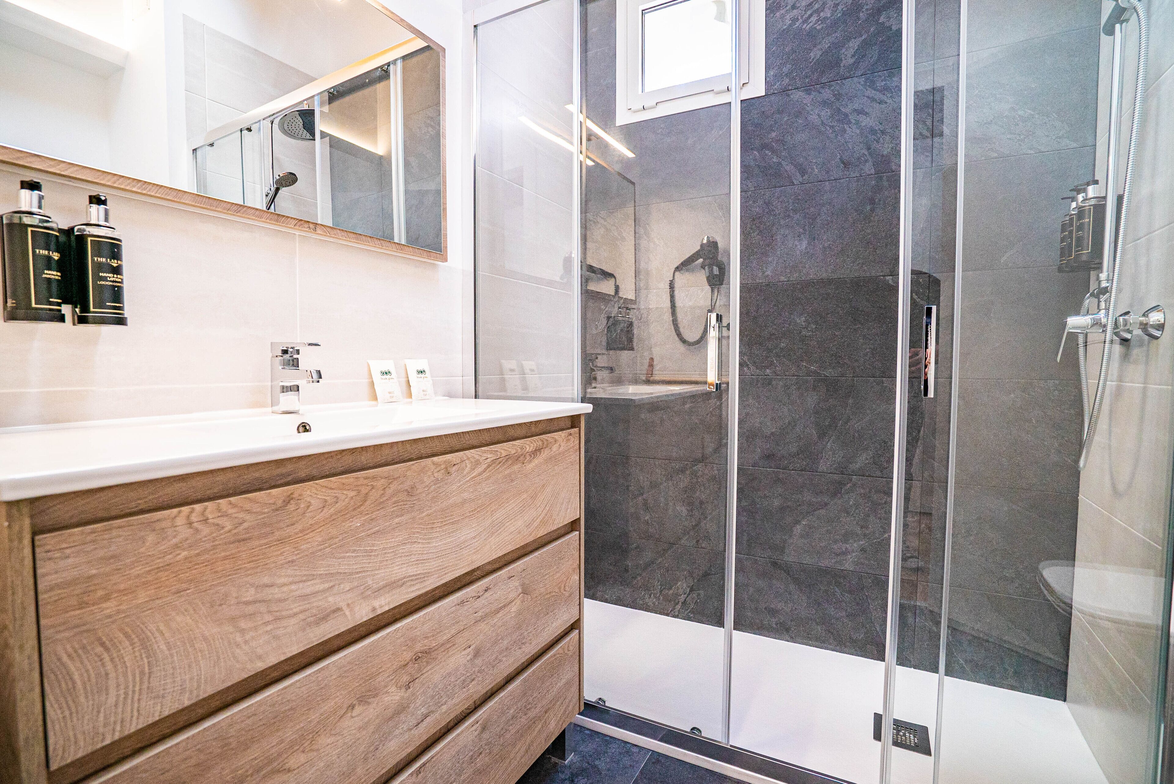 A modern bathroom with a wooden vanity, a glass shower enclosure, and a large mirror.