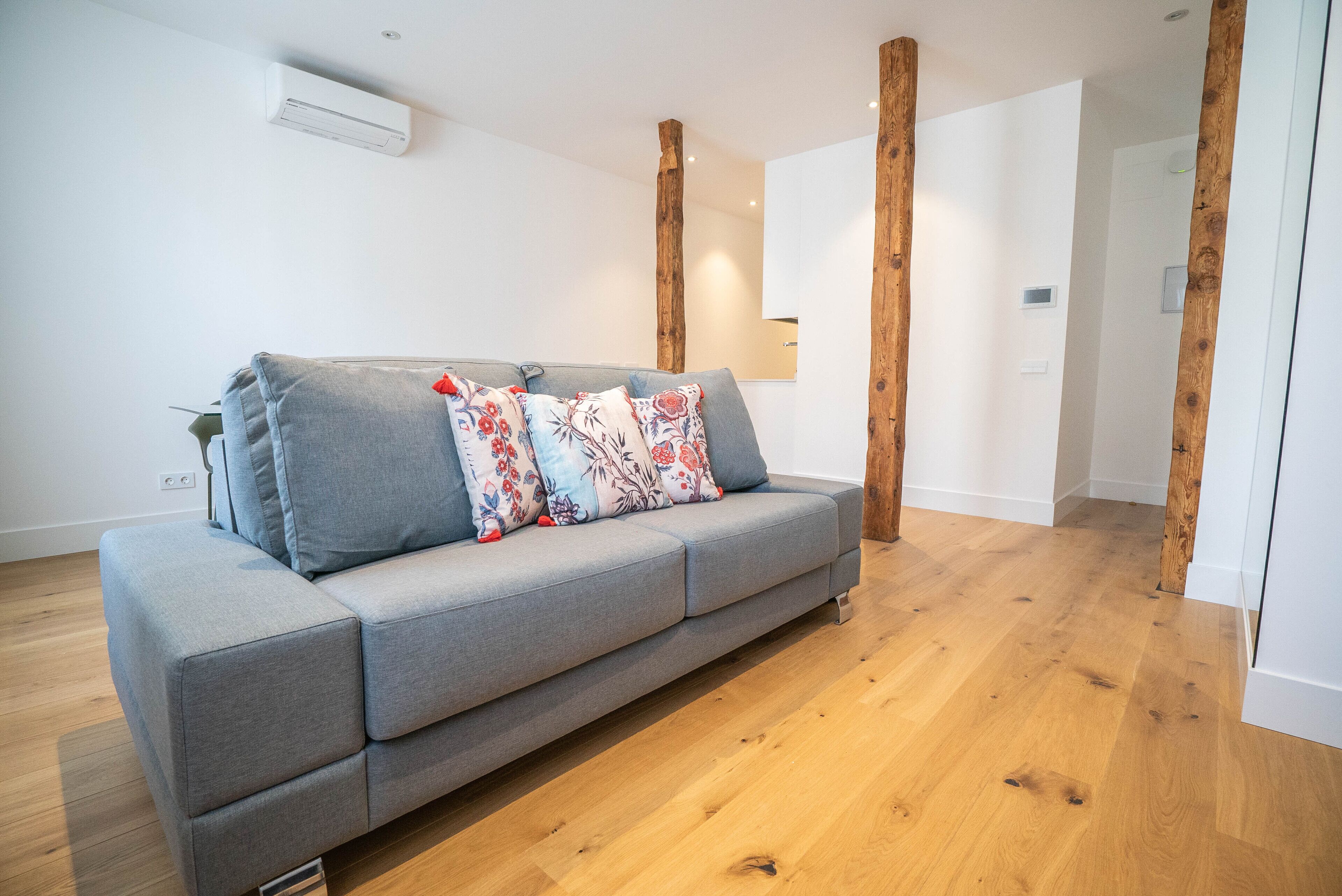 Un salon moderne avec un canapé gris, des poutres en bois et un plancher en bois.