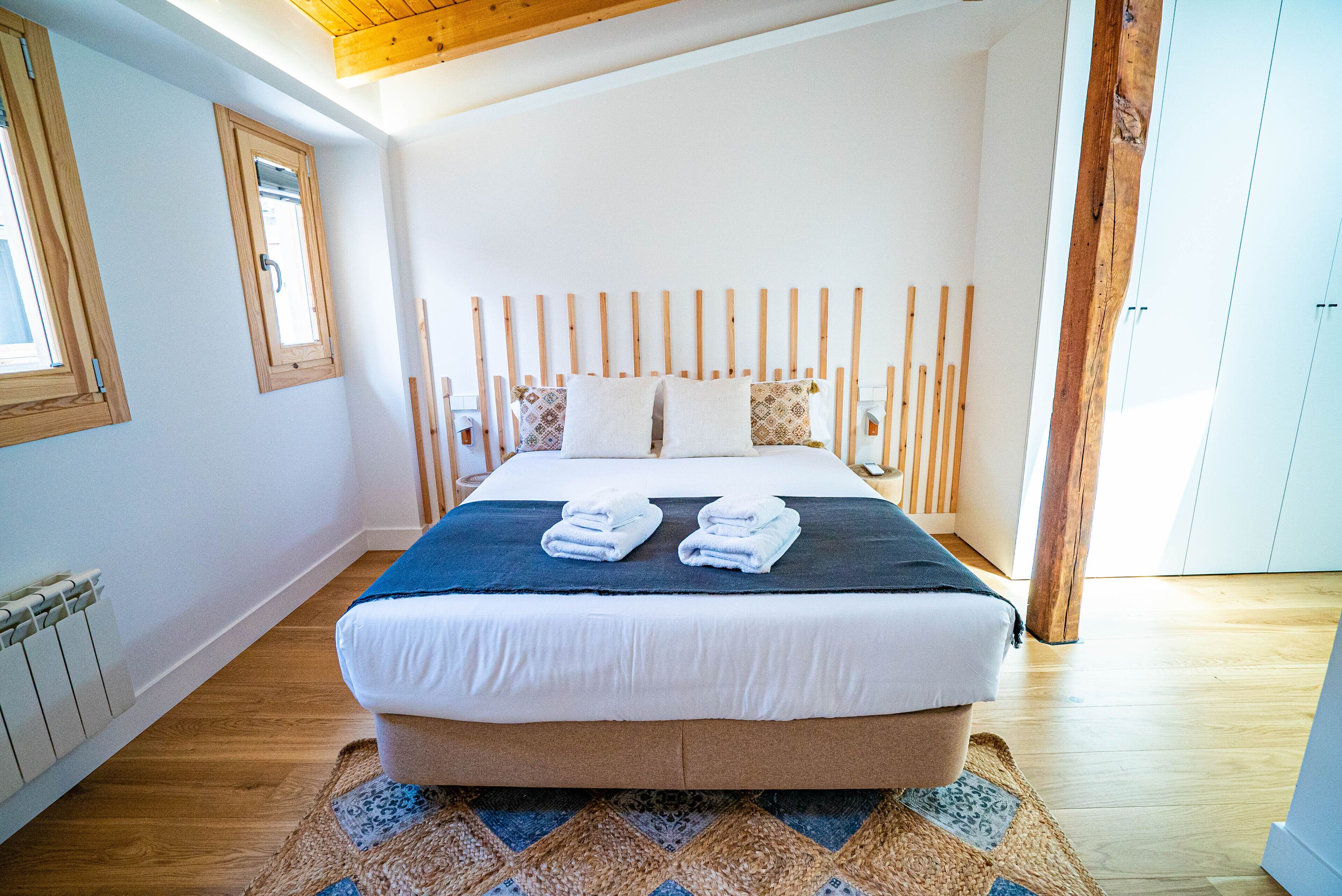 A neatly made bed with two towels, a wooden headboard, and a patterned rug.