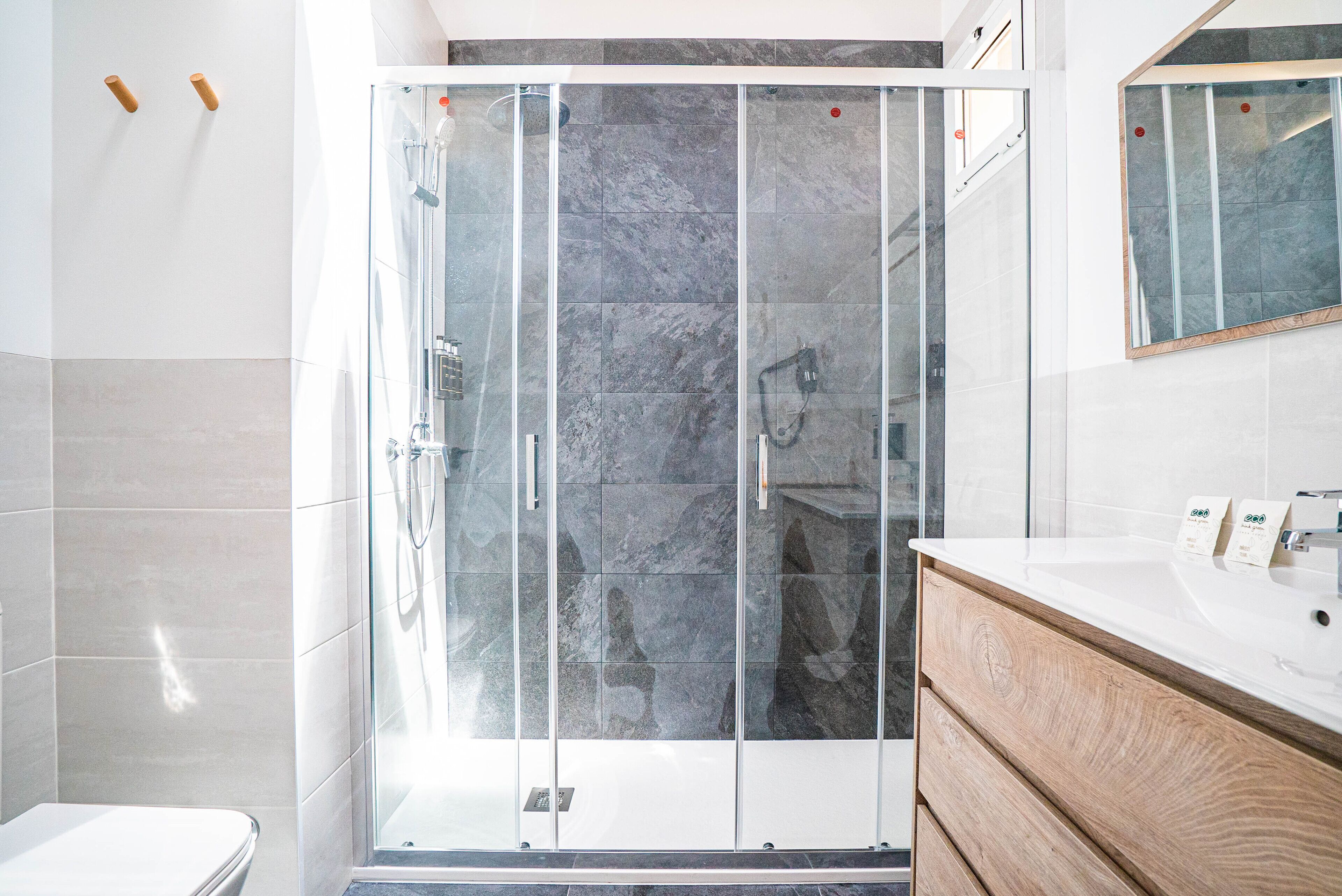 Un baño moderno con ducha de vidrio, tocador de madera y un espejo grande.