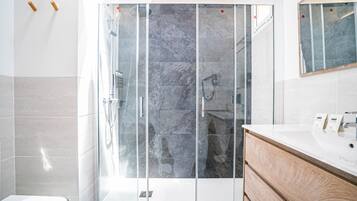 Un baño moderno con ducha de vidrio, tocador de madera y un espejo grande.