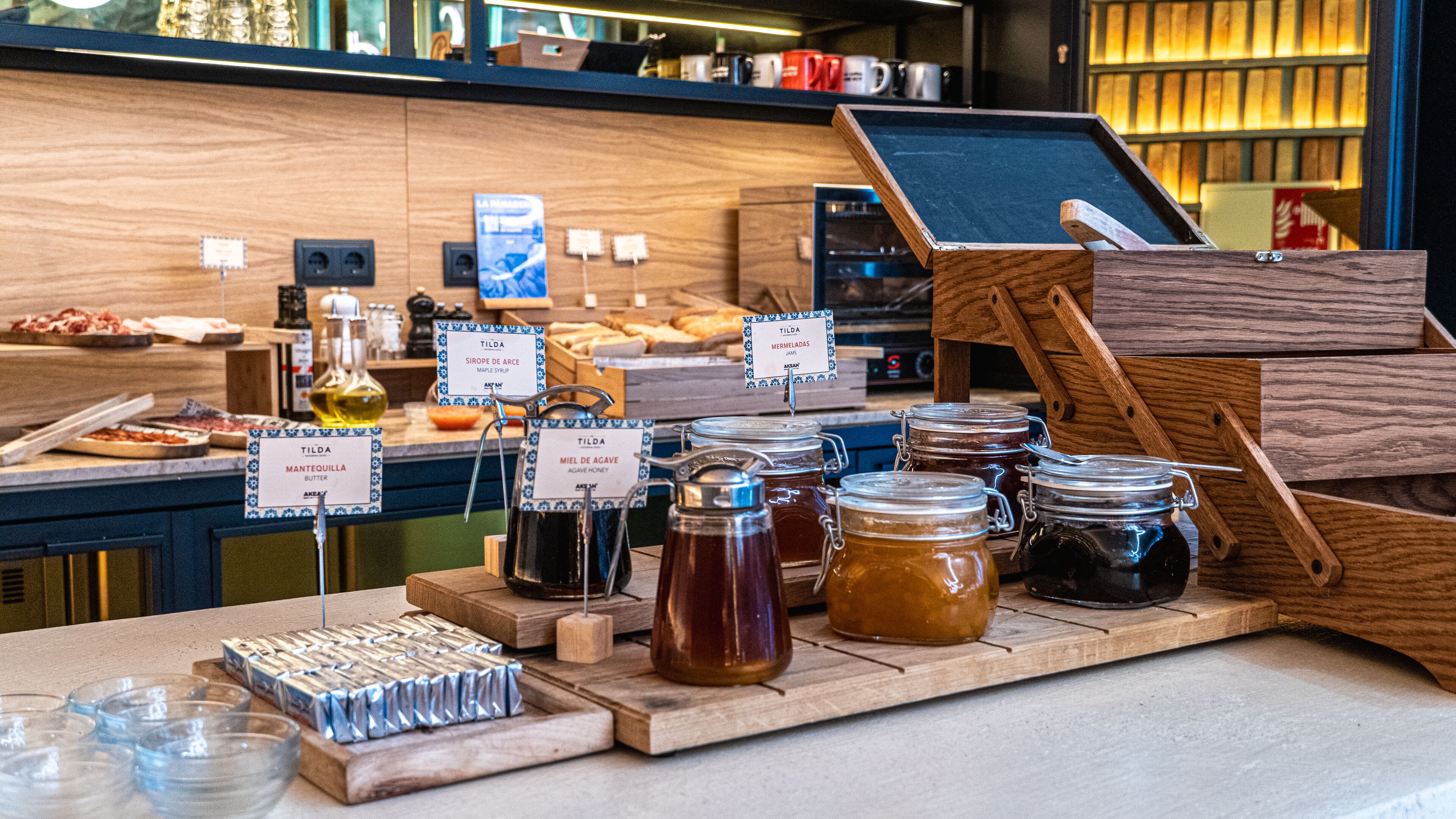A café counter with various jars of honey and maple syrup, a coffee machine, and a chalkboard menu.