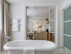 A modern bathroom with a freestanding bathtub, a glass shower enclosure, and a visible dining area through an open door.