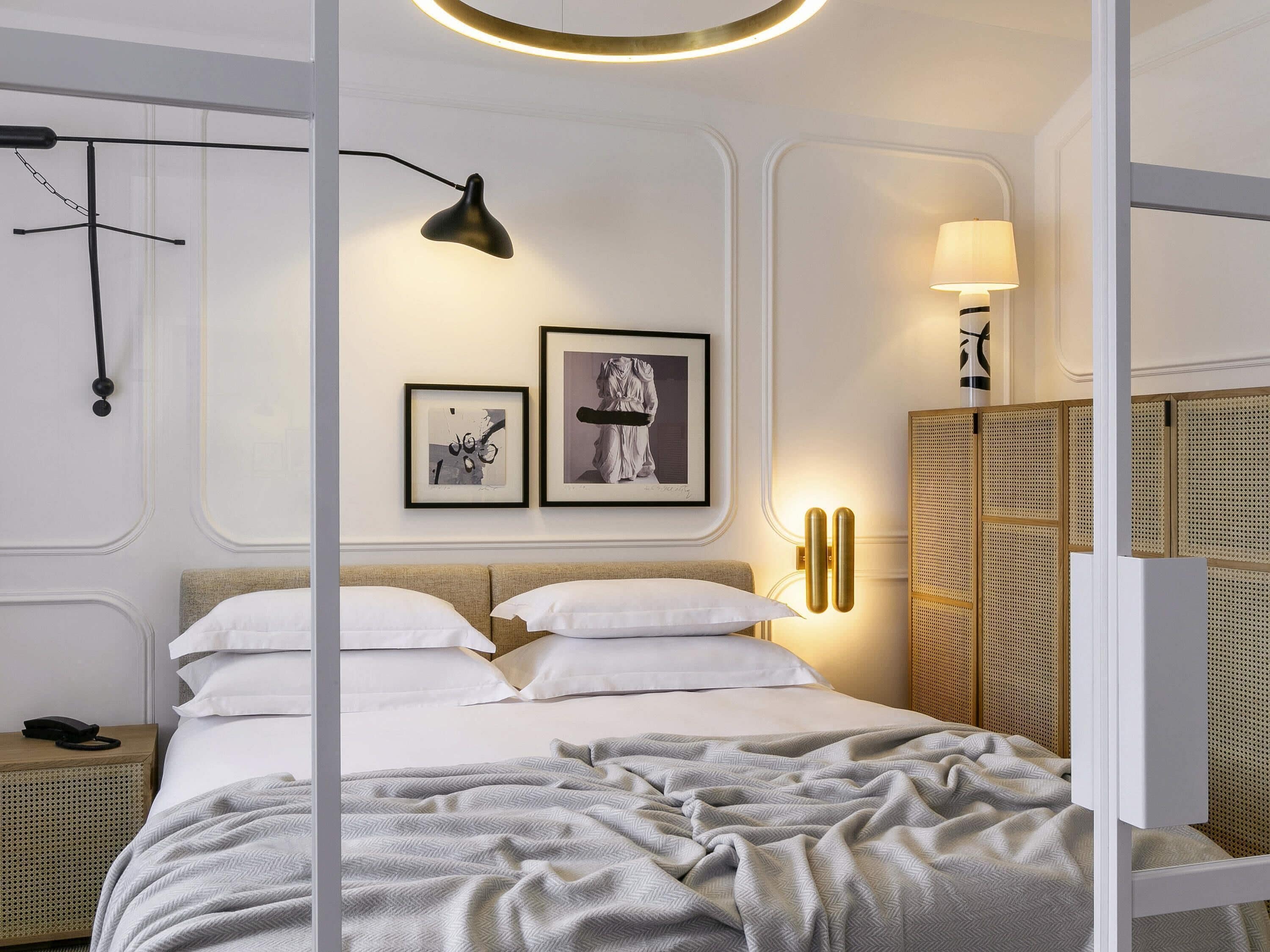 A modern bedroom with a bed, bedside tables, wall-mounted lamp, and framed artwork.