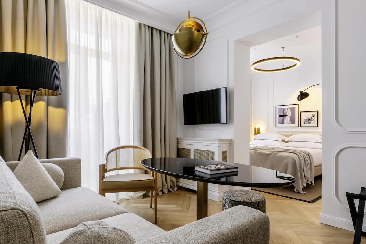Una habitación de hotel moderna con sofá, una mesa redonda, televisión, cama y chimenea.