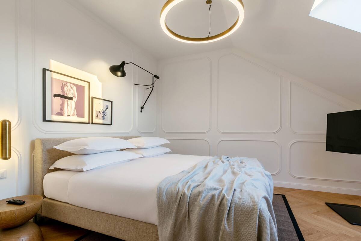 Un dormitorio con una cama, una mesita de noche, una lámpara, un televisor y cuadros en la pared.