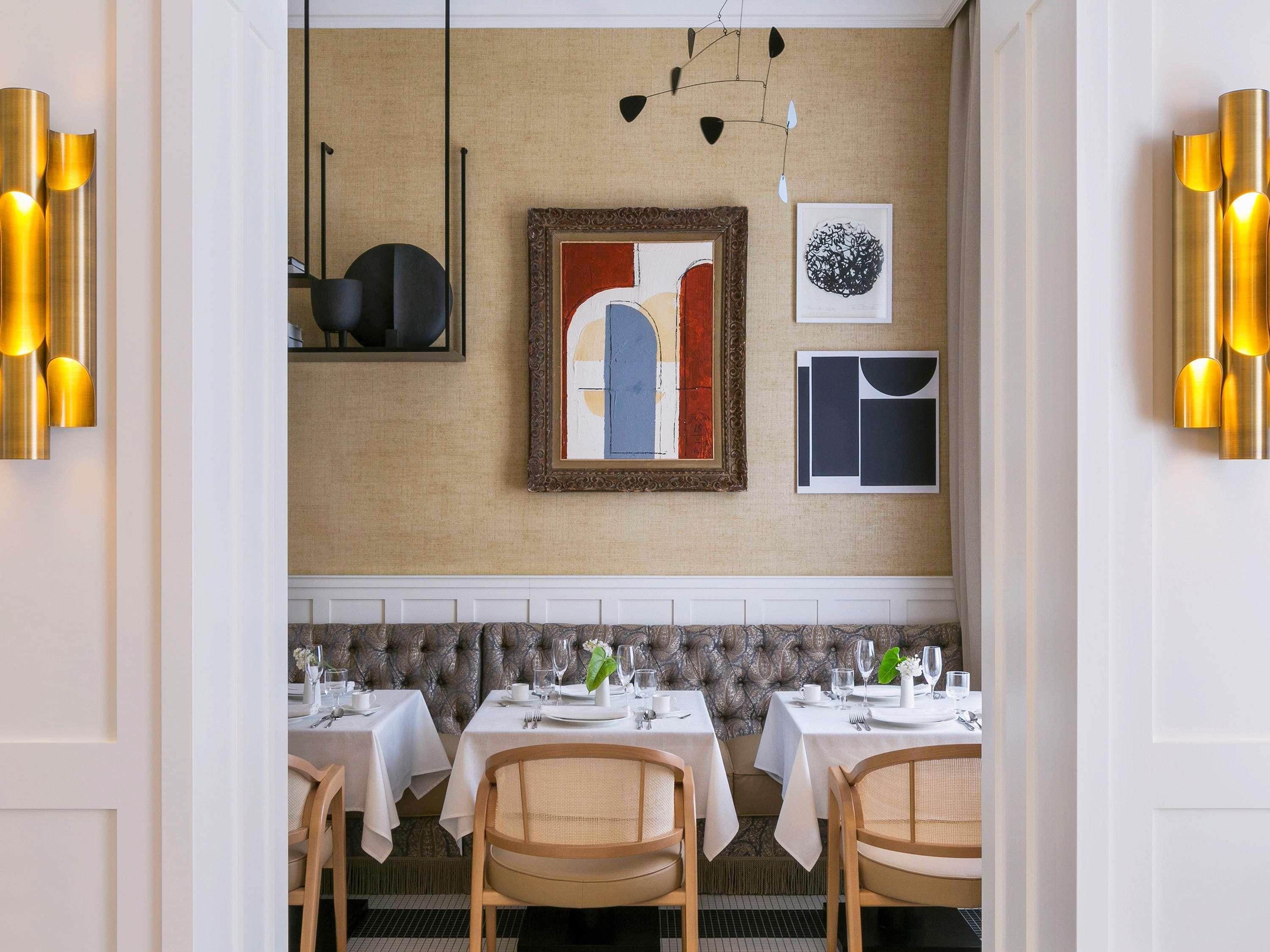 A dining area with tables set for service, a tufted wall, and wall-mounted light fixtures.