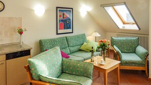 Ein gemütliches Wohnzimmer mit einer Couch, einem Sessel, einem kleinen Tisch mit Flasche und Gläsern sowie einem Bild an der Wand.