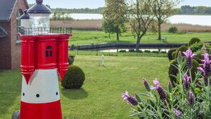 Ein roter und weißer Leuchtturm mit freiem Blick auf einen See und eine Brücke im Hintergrund.
