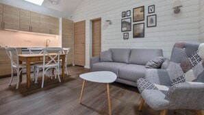 Een moderne keuken met houten kasten, een eettafel met stoelen, een grijze bank en een gestreept fauteuil.