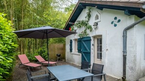 Een terras met een tafel en stoelen, een zwarte parasol, en een wit gebouw met groene luiken.