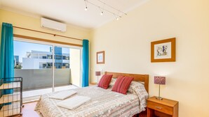 A bedroom with a bed, a nightstand, a lamp, and a view of the outside. - Apt. Casa Murrin, in a peaceful and secure complex with pool (Lagos)