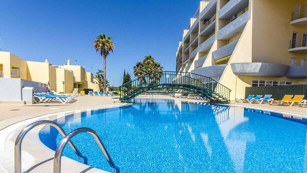 A clear blue pool with a bridge, lounge chairs, and palm trees. - Apt. Casa Murrin, in a peaceful and secure complex with pool (Lagos)