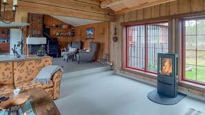 A cozy cabin interior with a fireplace, wooden walls, a sofa, and a dining area.