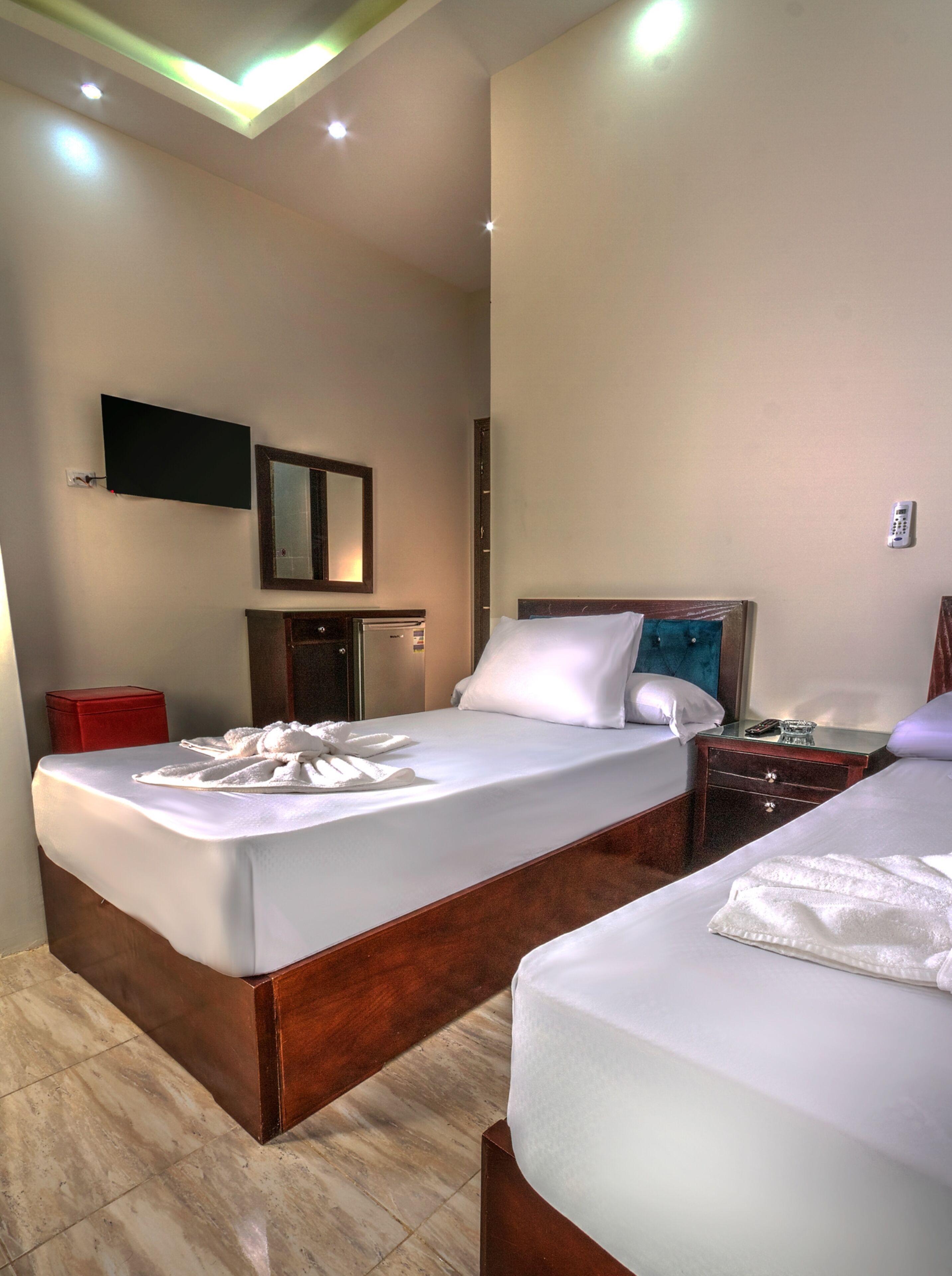 A hotel room with two beds, a TV mounted on the wall, a bedside table with a phone, and a red suitcase on the floor.