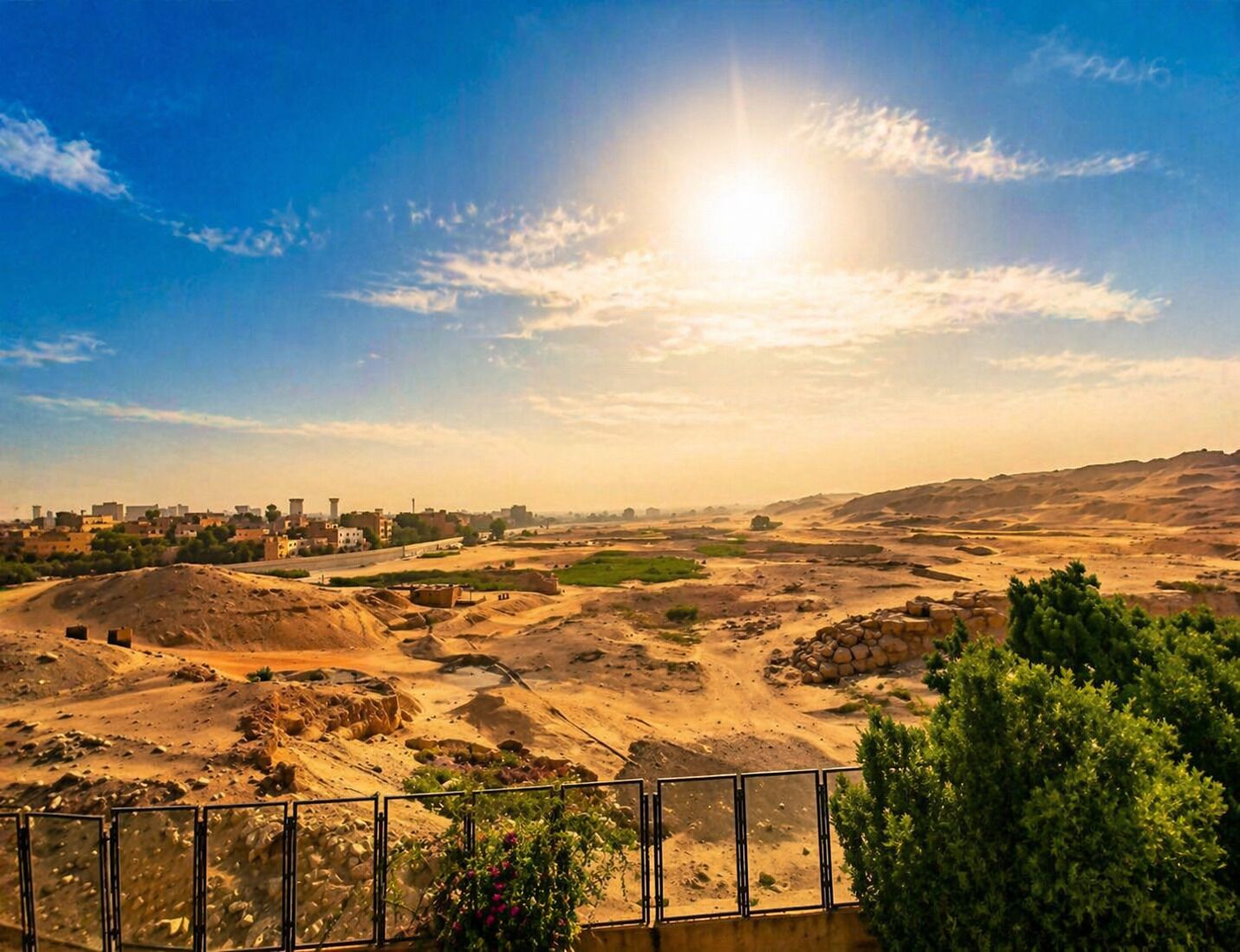 A desert landscape with a city in the distance, a clear sky, and a fence in the foreground.