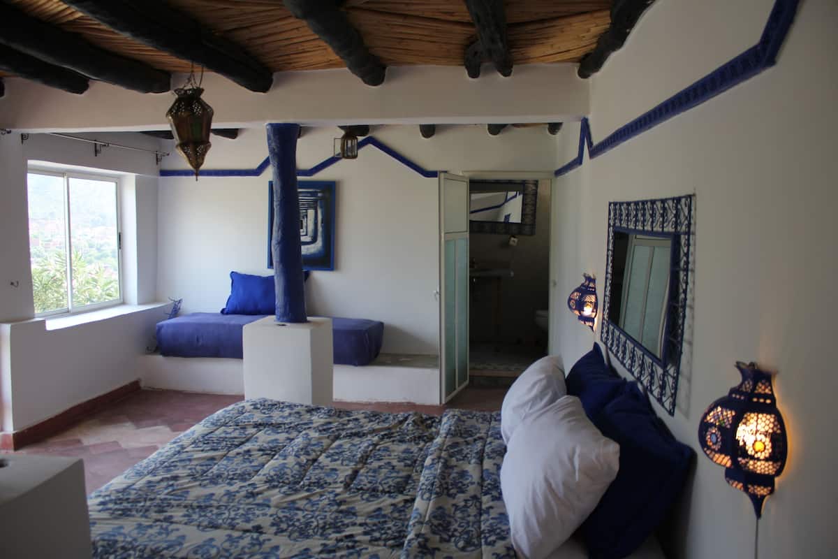 Un dormitorio con cama, ventana, pared azul y lámpara colgante.