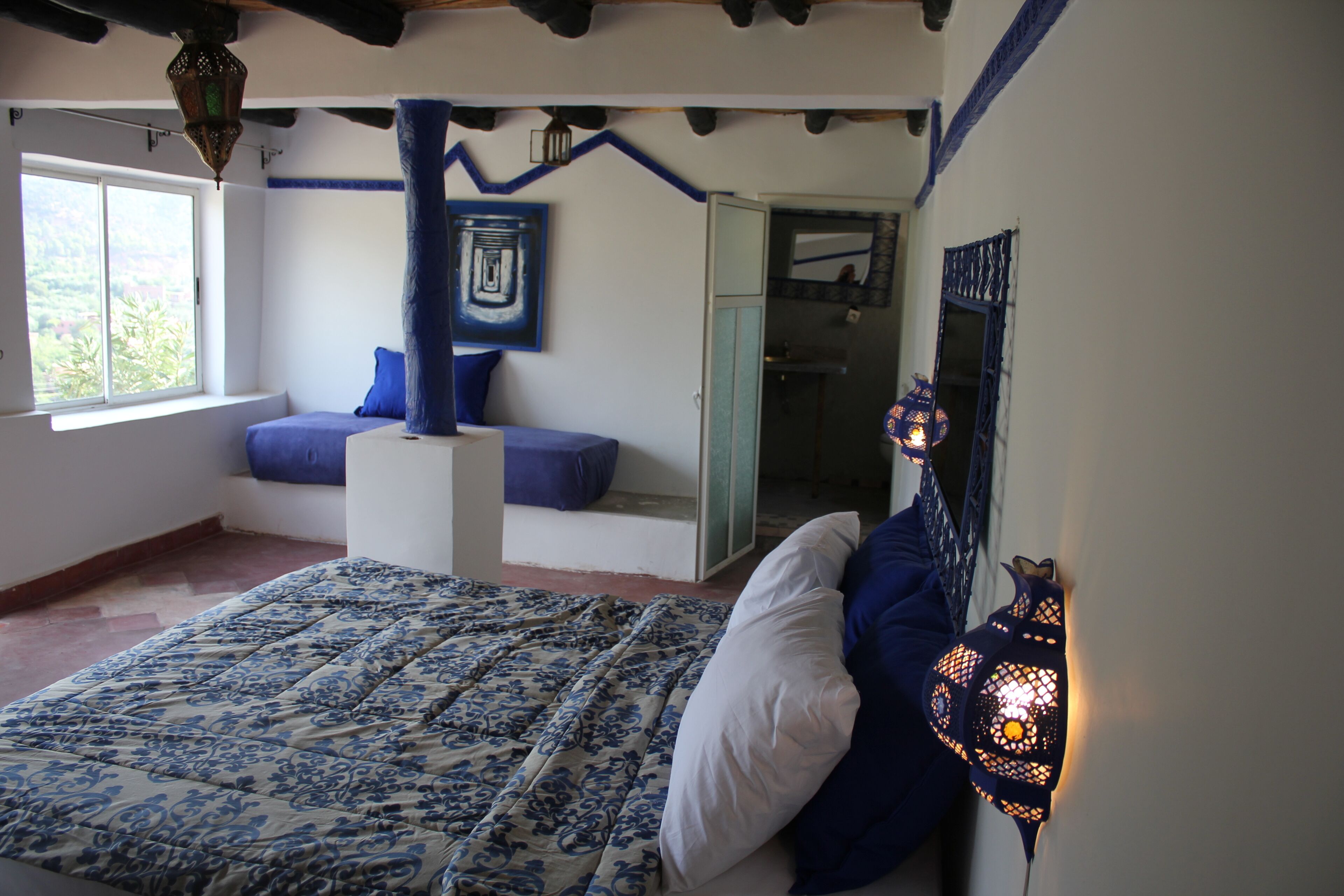 A bedroom with a bed, a window, a blue wall, and a door leading to another room.