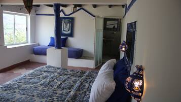 A bedroom with a bed, a window, a blue wall, and a door leading to another room.
