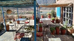 An outdoor patio with tables and chairs, surrounded by potted plants, set against a mountainous backdrop. - Kasbah de Ouirgane (Ouirgane)