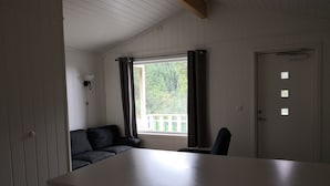Una habitación con techo blanco, ventana con cortinas, puerta con mirilla y un área de kitchenette.