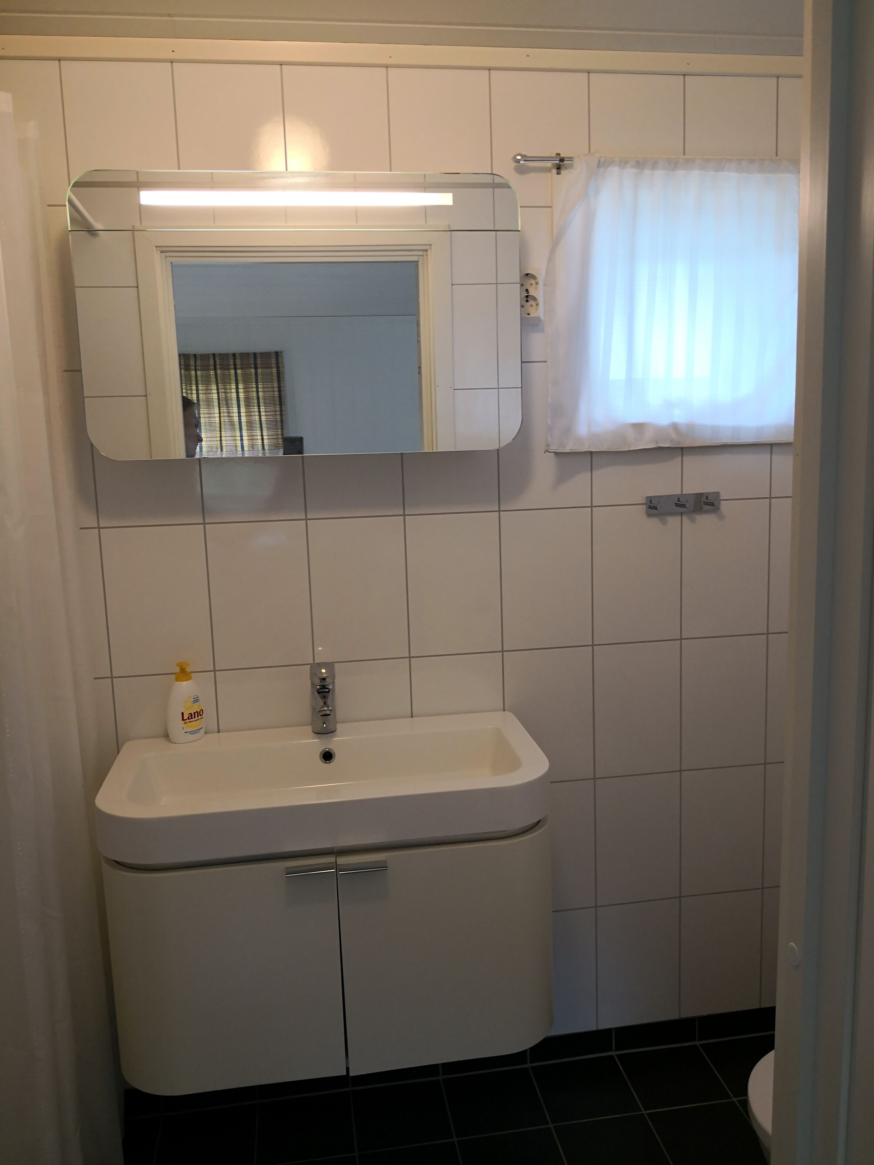 A bathroom with a white sink, mirror, and a window with a white curtain.