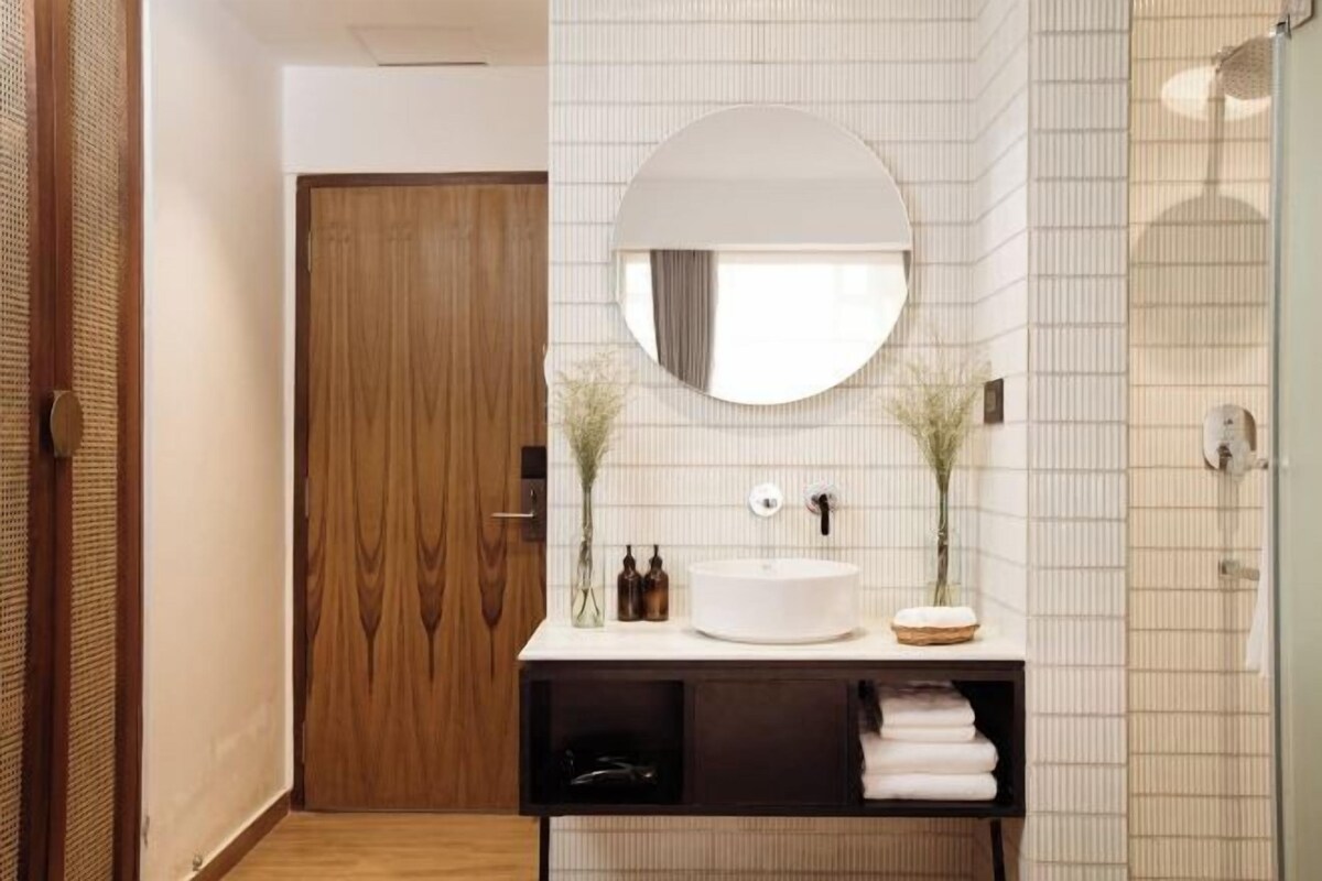 A modern bathroom with a wooden door, a round mirror, a white sink, and a towel rack.