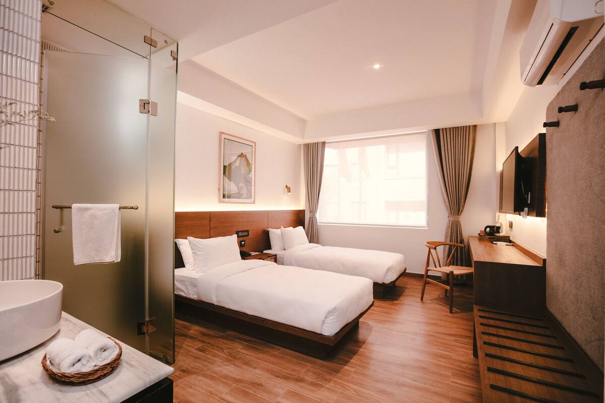 A hotel room with two beds, a bathroom, a desk, and a large window.