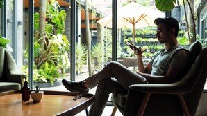 A man sitting in a modern lounge area with large windows, a coffee table, and indoor plants. - Nomad Hotel (Kathmandu)