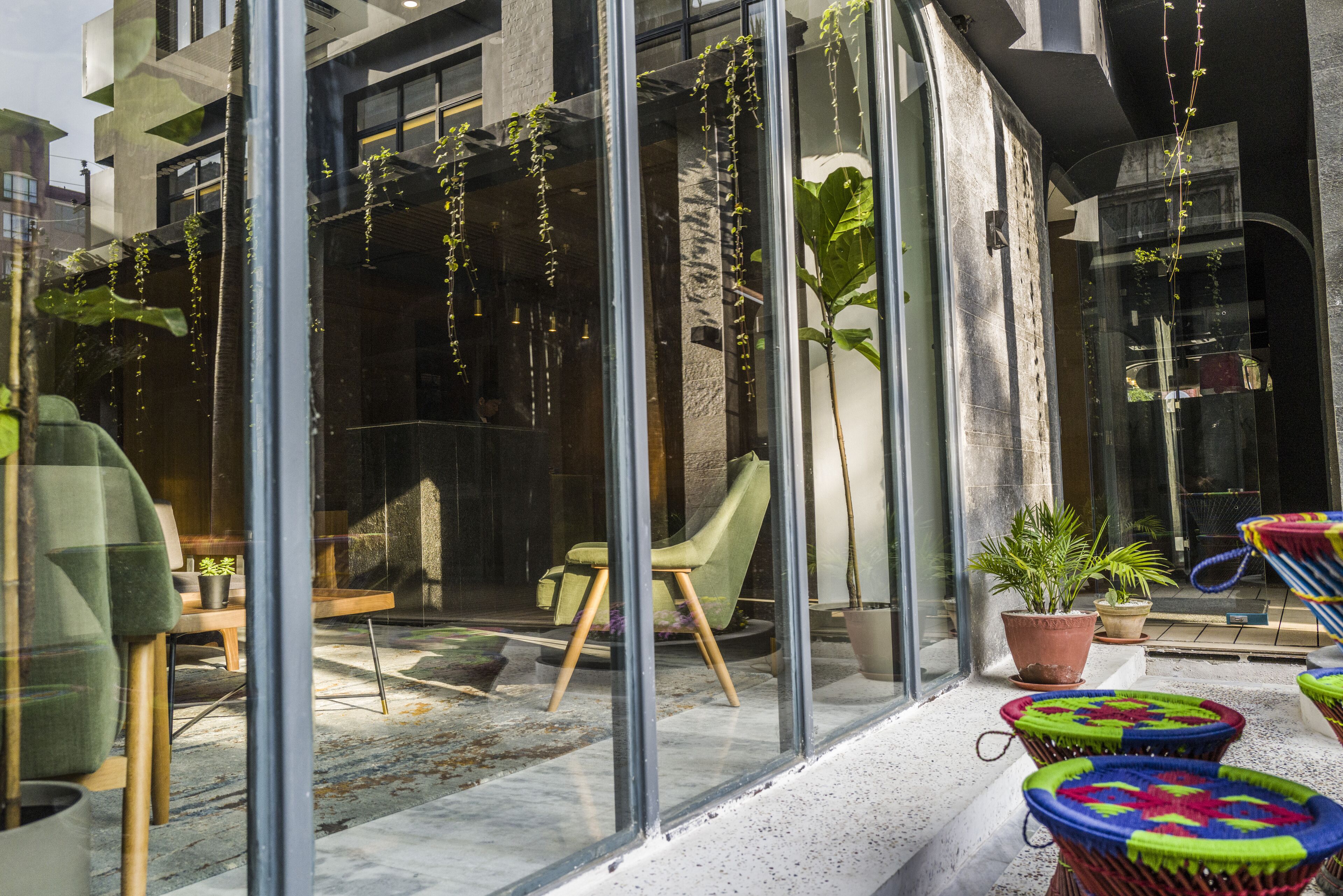 Un espacio exterior moderno con paredes de vidrio, una silla verde y plantas en macetas.