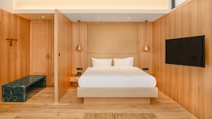 A modern bedroom with a large bed, wooden walls, a flat-screen TV, and a bench. - Nomad Hotel (Kathmandu)