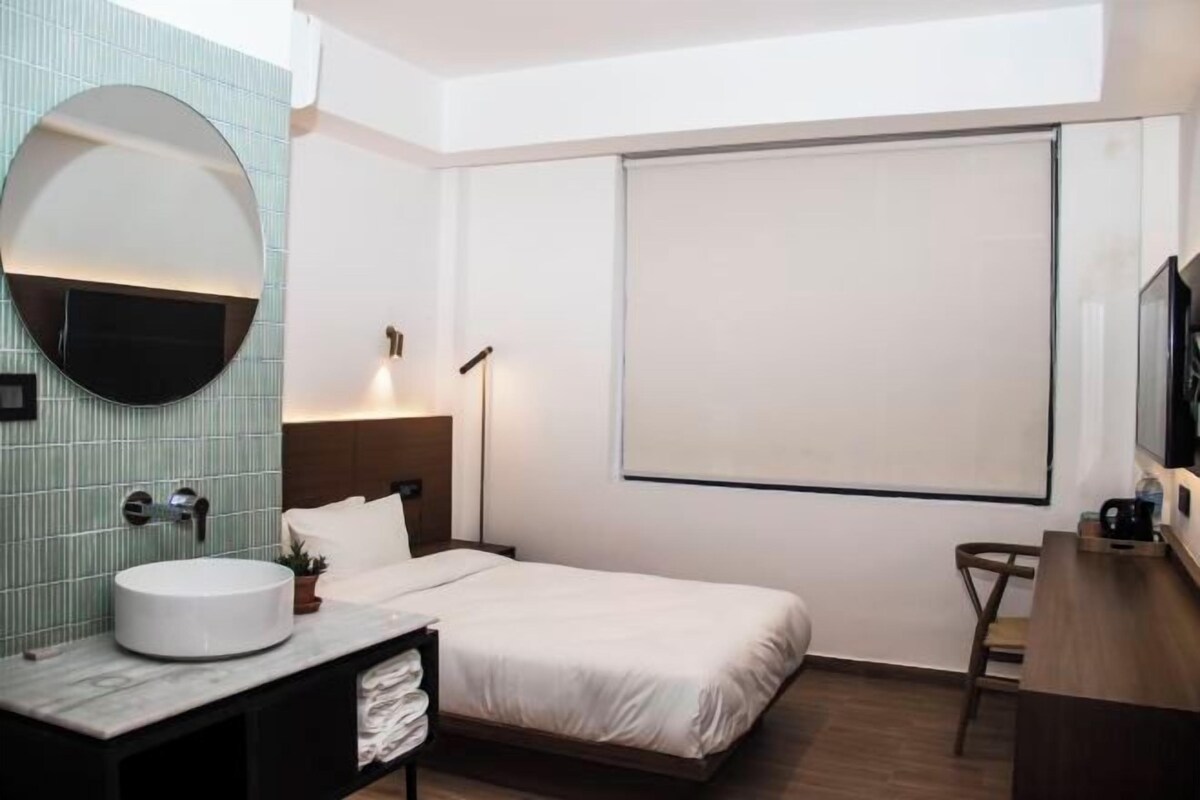 A hotel room with a round mirror, a bed, a desk, and a television.