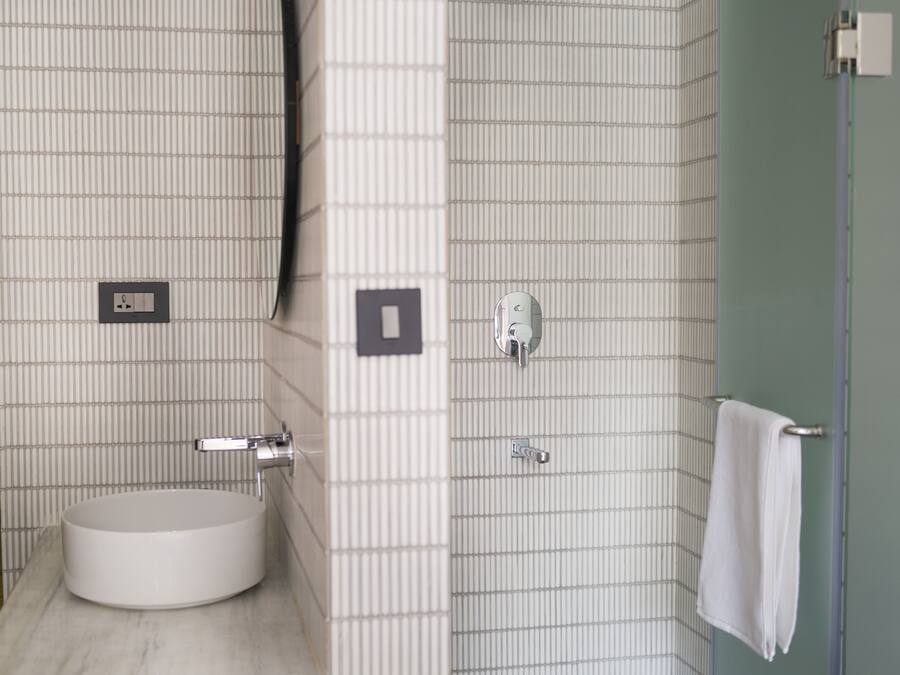 Casa de banho com lavatório branco, espelho, chuveiro e barra para toalhas.